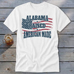 White t-shirt with "Alabama Raised American Made" text over a distressed American flag.