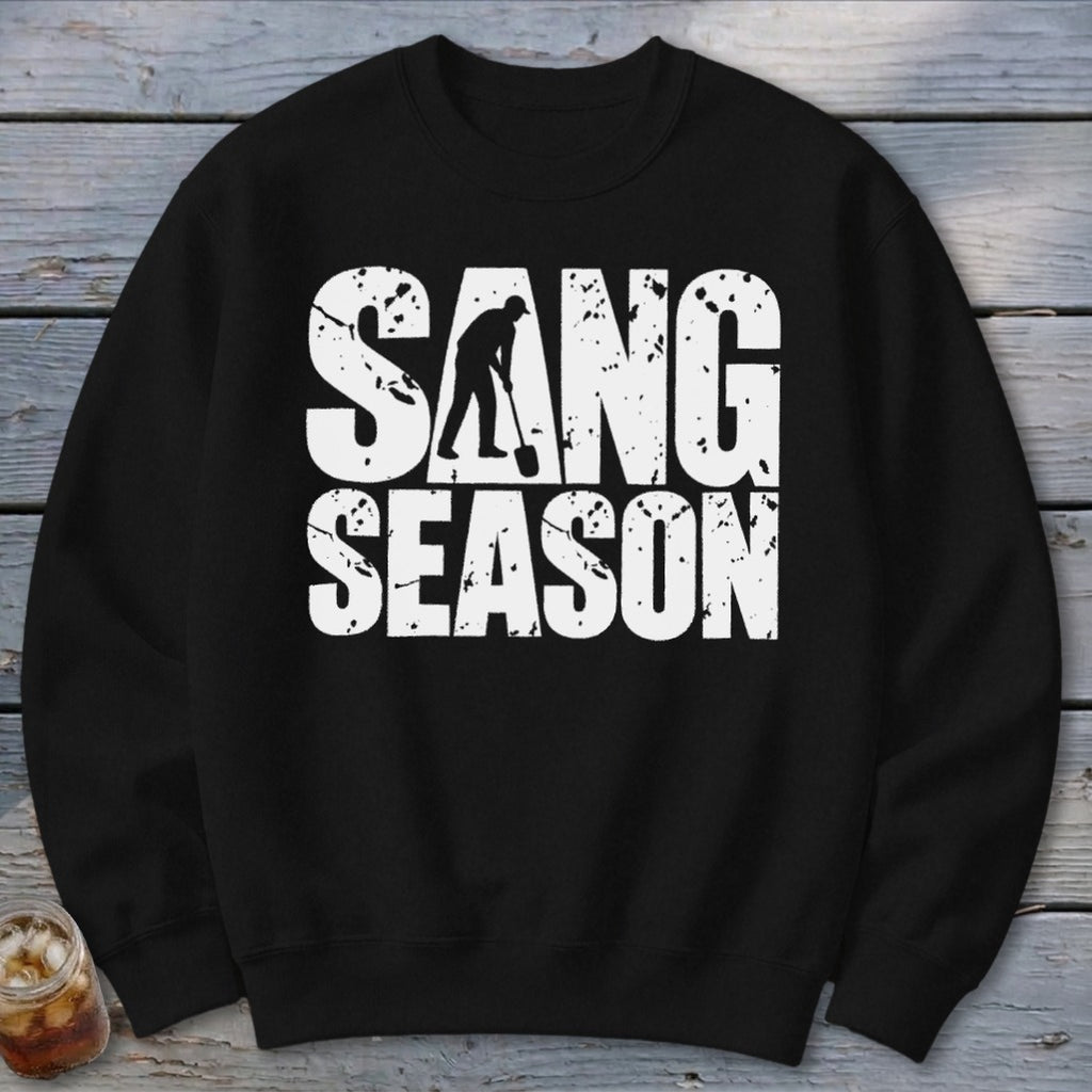 A black long-sleeved crewneck sweatshirt with white distressed text that reads SANG SEASON, featuring a person digging with a shovel inside the letter A.