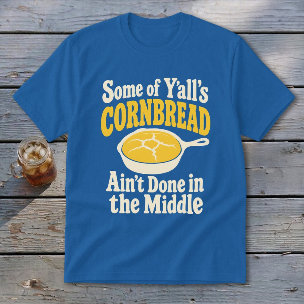 Blue t-shirt featuring a graphic of a skillet with cornbread and text reading Some of Y'all's Cornbread Ain't Done in the Middle.