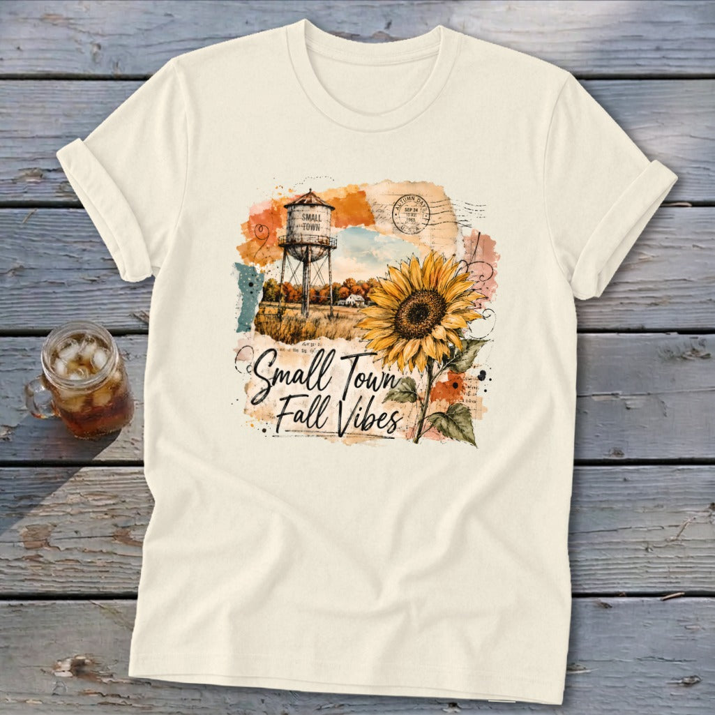 Cream t-shirt with "Small Town Fall Vibes" graphic featuring a sunflower and water tower.