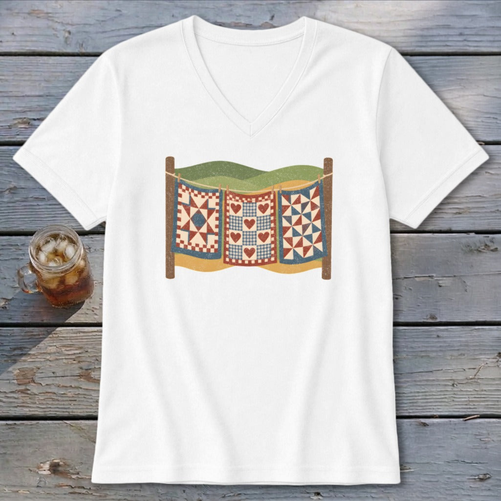 White V-neck t-shirt featuring a retro graphic of three colorful quilts hanging on a clothesline against a wooden background.