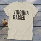 Cream t-shirt with "Virginia Raised" text in dark gray, next to a glass of iced tea.