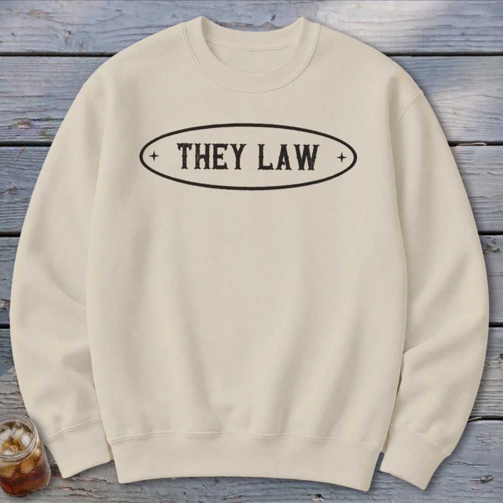 Cream sweatshirt with black oval graphic displaying "THEY LAW" text.