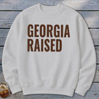 White sweatshirt with "GEORGIA RAISED" printed in brown on the chest.
