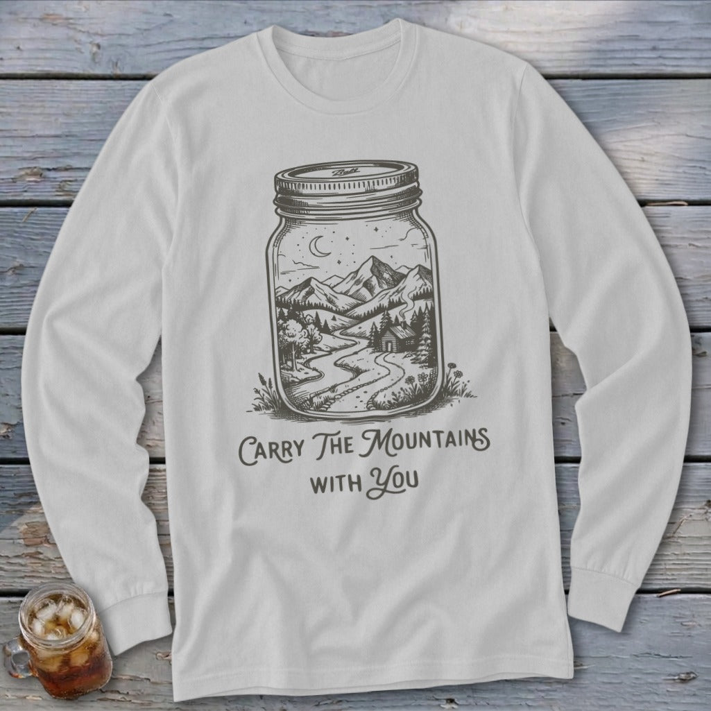 A light gray long-sleeve t-shirt featuring a line drawing of mountains inside a mason jar with the text "Carry The Mountains With You."