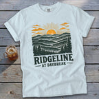 White t-shirt with "RIDGELINE AT DAYBREAK" text and sunrise mountain landscape graphic.