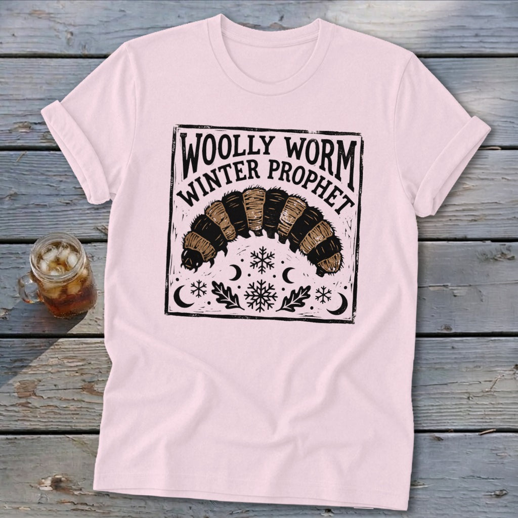 Light pink crewneck t-shirt featuring a black block-print graphic of a woolly worm and text reading Woolly Worm Winter Prophet.