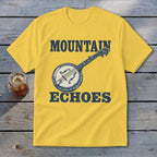 A yellow t-shirt with a vintage banjo graphic and the text MOUNTAIN ECHOES resting on a wooden surface.