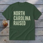 Green t-shirt with "NORTH CAROLINA RAISED" text in cream lettering.