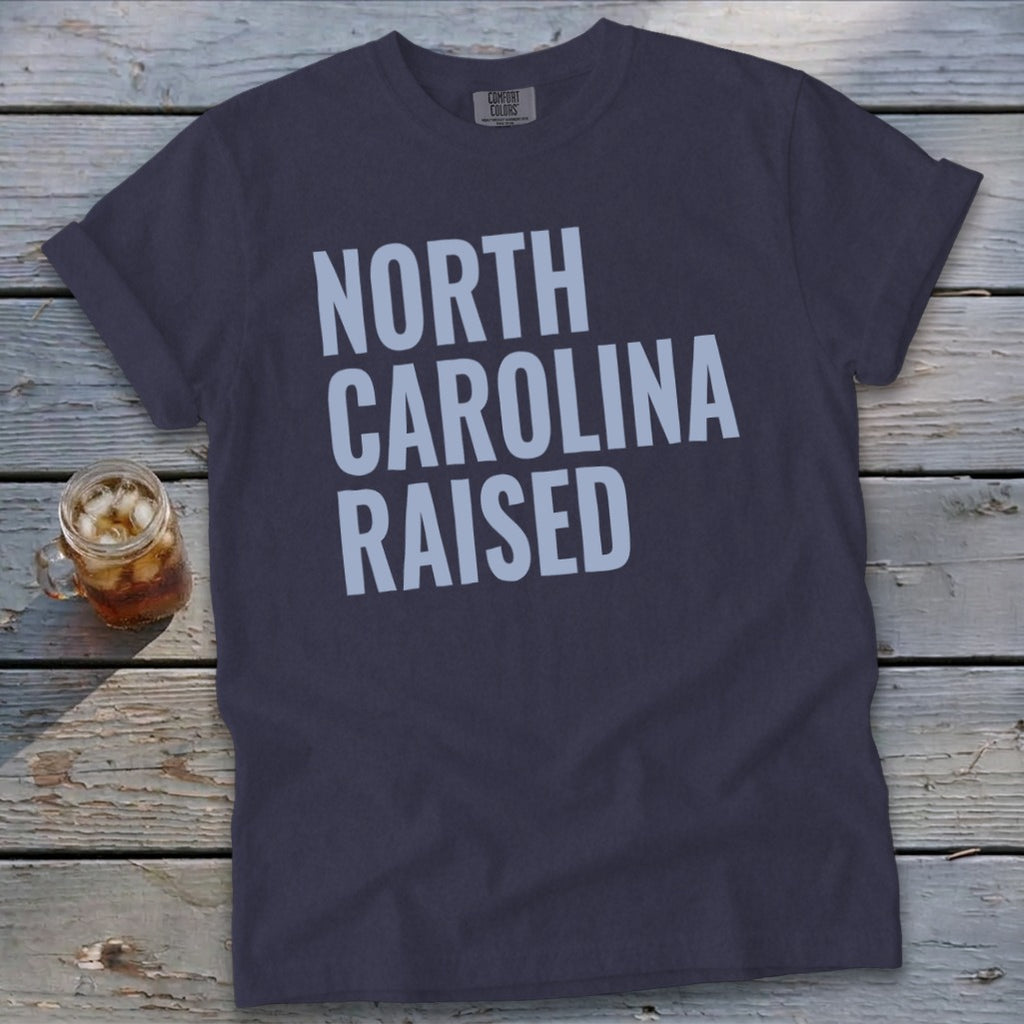 Dark grey t-shirt with "NORTH CAROLINA RAISED" text in light blue.