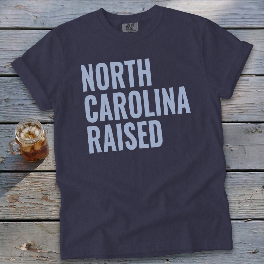 Dark grey t-shirt with "NORTH CAROLINA RAISED" text in light blue.