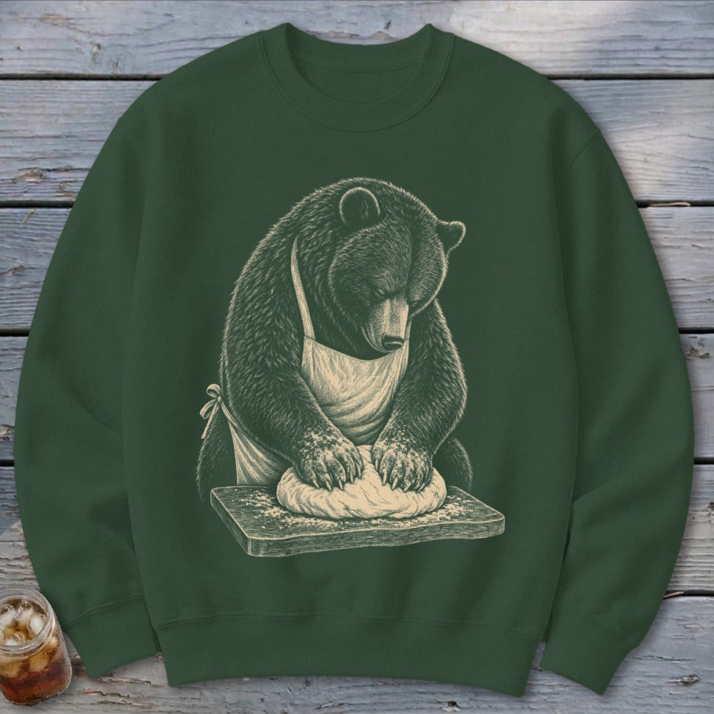 Bear wearing an apron kneading dough on a wooden cutting board.