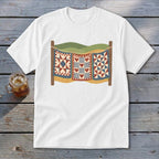 A white t-shirt featuring a graphic of three colorful quilts hanging on a clothesline against a landscape.