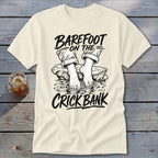 Cream t-shirt with text "BAREFOOT ON THE CRICK BANK" and illustration of bare feet in water.