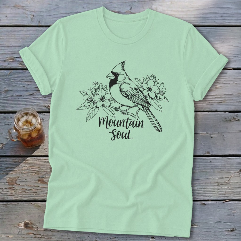 Light green t-shirt with a black ink drawing of a cardinal and flowers, text reads "Mountain Soul".