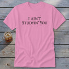 Pink t-shirt with "I AIN'T STUDYIN' YOU" text and a glass of iced beverage.