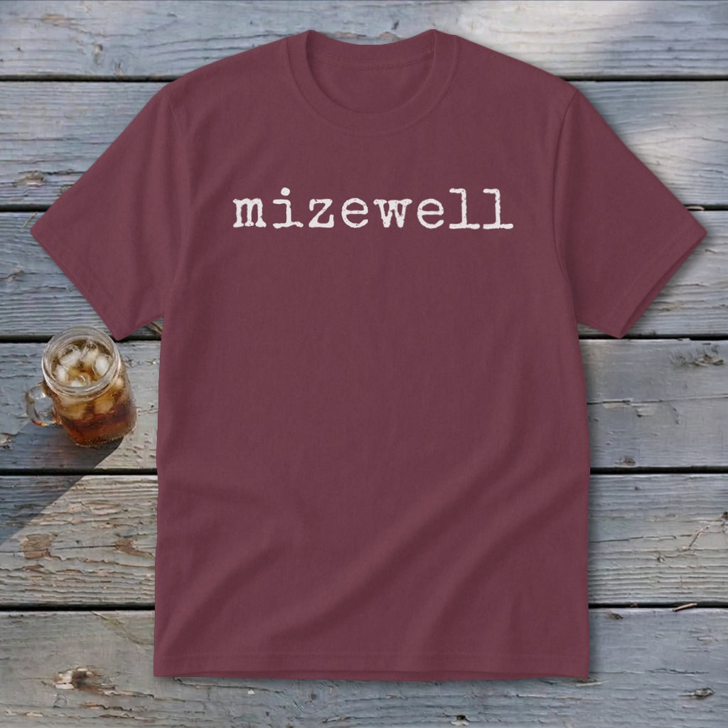 Burgundy t-shirt with "mizewell" in white typewriter font, next to a glass of iced tea.