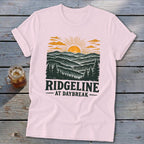 Pink t-shirt with a graphic of a sunrise over mountains, text "RIDGELINE AT DAYBREAK".