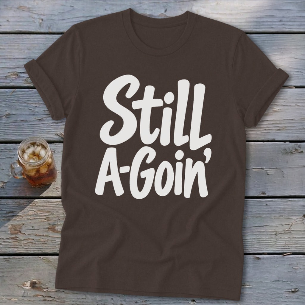A brown short-sleeve t-shirt with rolled cuffs and white text that reads Still A-Goin'.