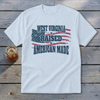 A white t-shirt featuring a distressed American flag and text that reads West Virginia Raised American Made.