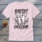 Pink t-shirt with black graphic of bare feet in water and text "Barefoot On The Creek Bank".
