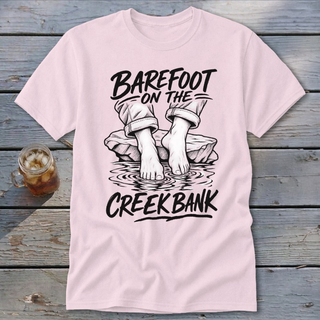 Pink t-shirt with black graphic of bare feet in water and text "Barefoot On The Creek Bank".