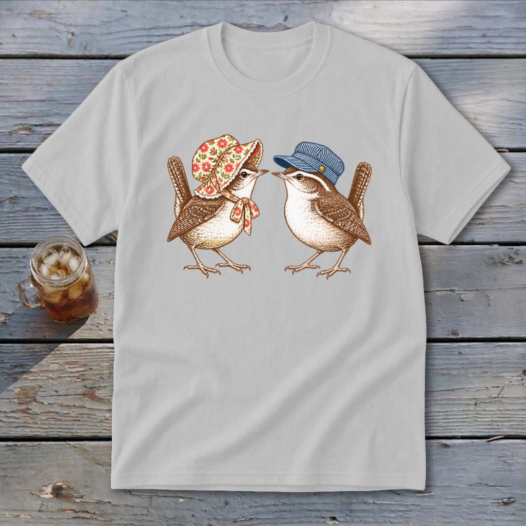 Two wrens, one with a bonnet and the other with a cap, face each other on a light grey t-shirt.