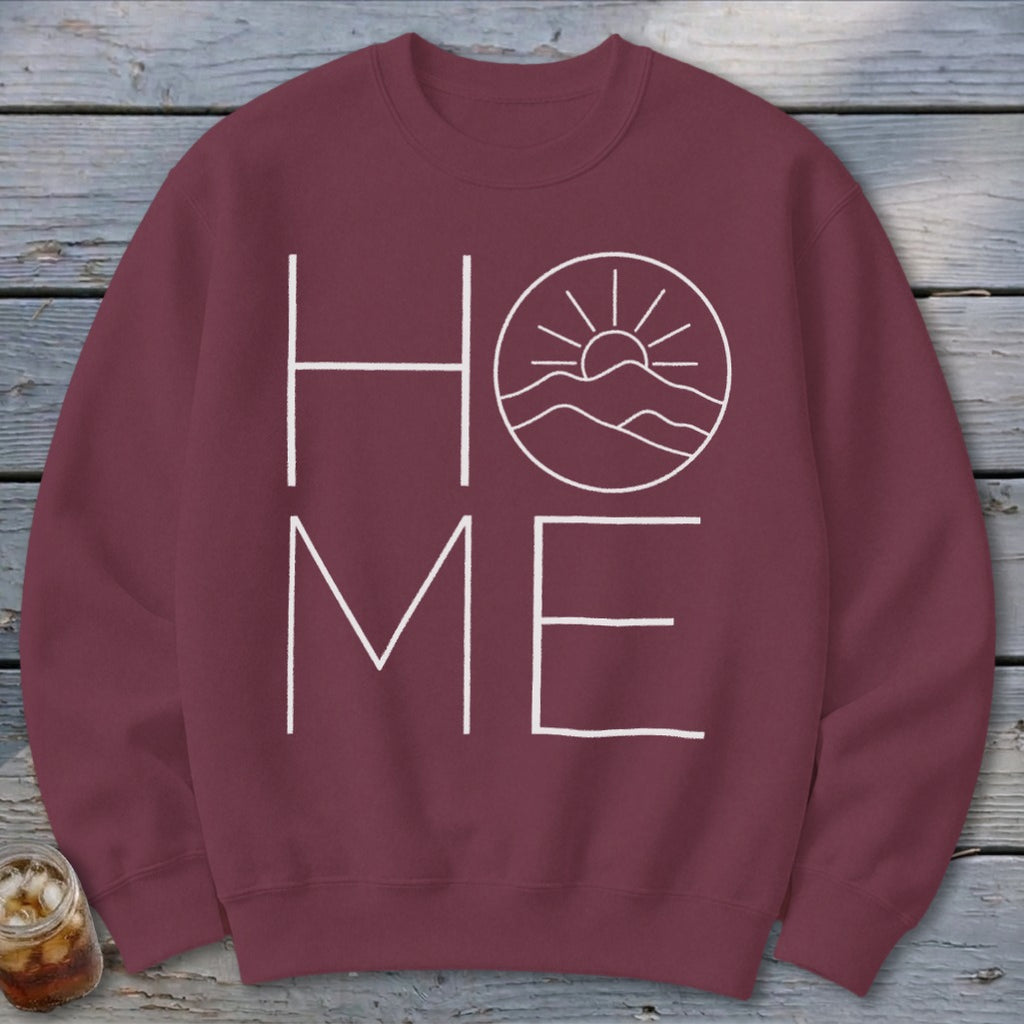 Maroon crewneck sweatshirt featuring a white graphic with the word HOME, where the O is replaced by a mountain landscape and sun.