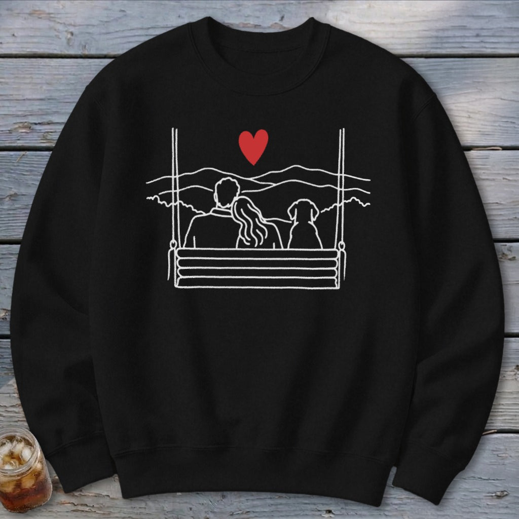 Black sweatshirt with white line art of couple and dog on a swing under a red heart.