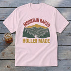 Light pink t-shirt with retro mountain landscape graphic and text reading MOUNTAIN RAISED HOLLER MADE.