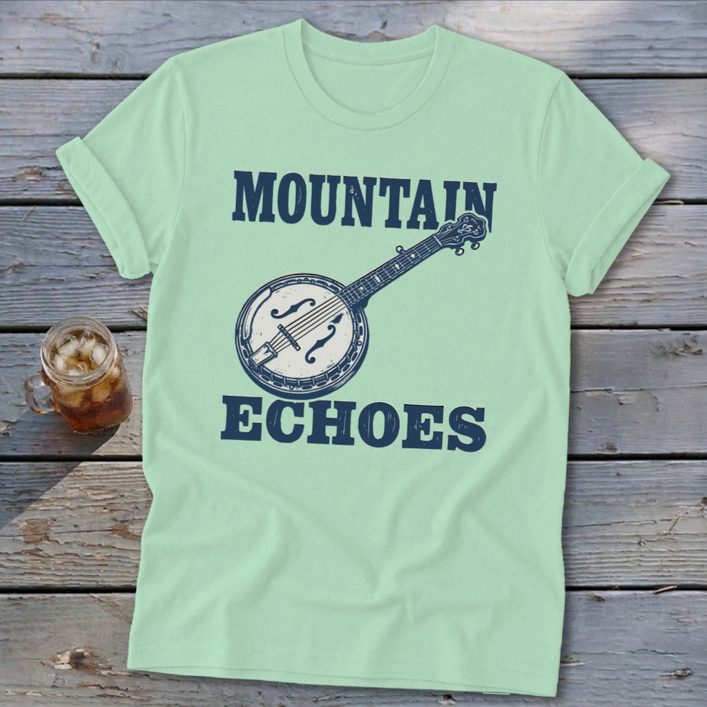 Light green t-shirt with a vintage banjo graphic and text reading Mountain Echoes, laid on wood.
