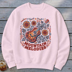 Light pink crewneck sweatshirt featuring a colorful graphic of a guitar, sunflowers, and the text Mountain Melodies.