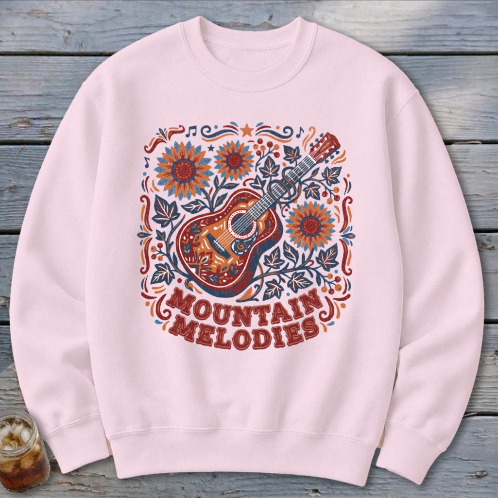 Light pink crewneck sweatshirt featuring a colorful graphic of a guitar, sunflowers, and the text Mountain Melodies.