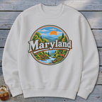 White sweatshirt featuring a circular Maryland graphic with mountains, river, trees, and a deer.