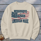 Cream-colored crewneck sweatshirt featuring a distressed American flag graphic with the text Mississippi Raised American Made.