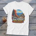 White t-shirt with scenic mountain overlook graphic and text "Peak weekend. Same playlist. New overlook."