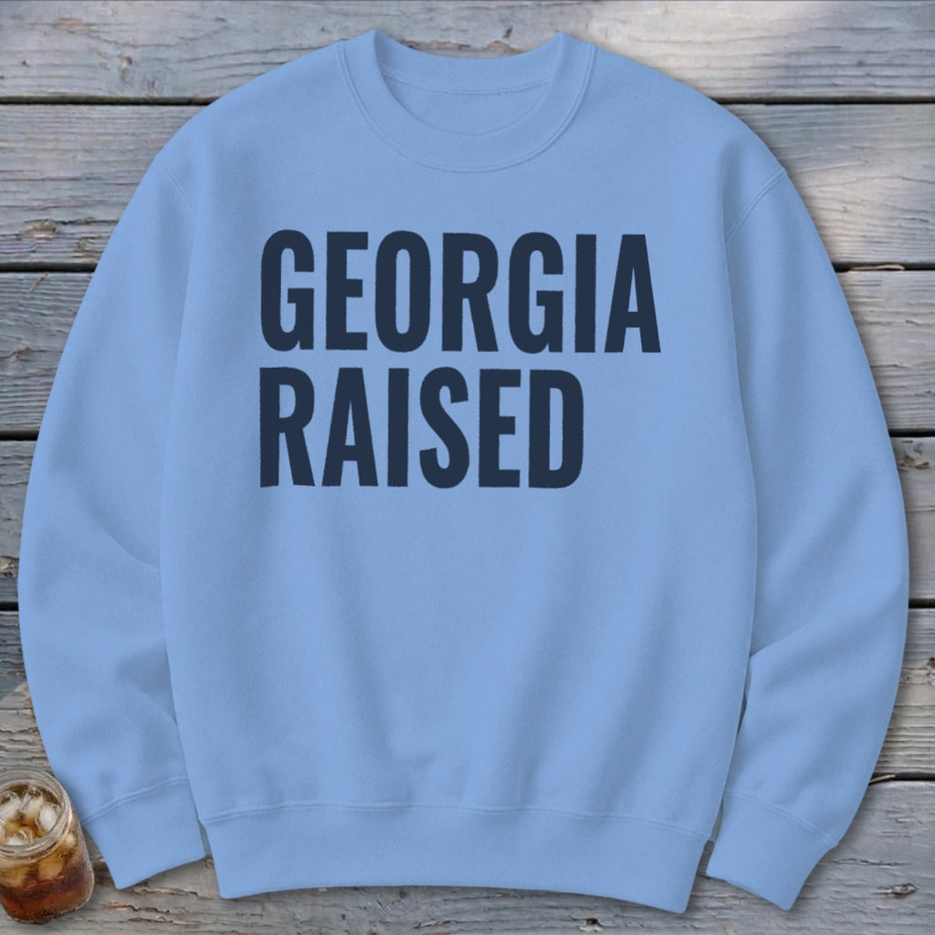 Light blue crewneck sweatshirt with navy blue text "GEORGIA RAISED"