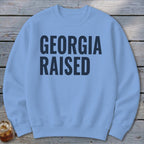 Light blue crewneck sweatshirt with navy blue text "GEORGIA RAISED"