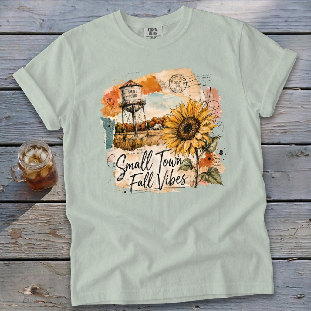 Light blue t-shirt with "Small Town Fall Vibes" graphic featuring a water tower and sunflower.