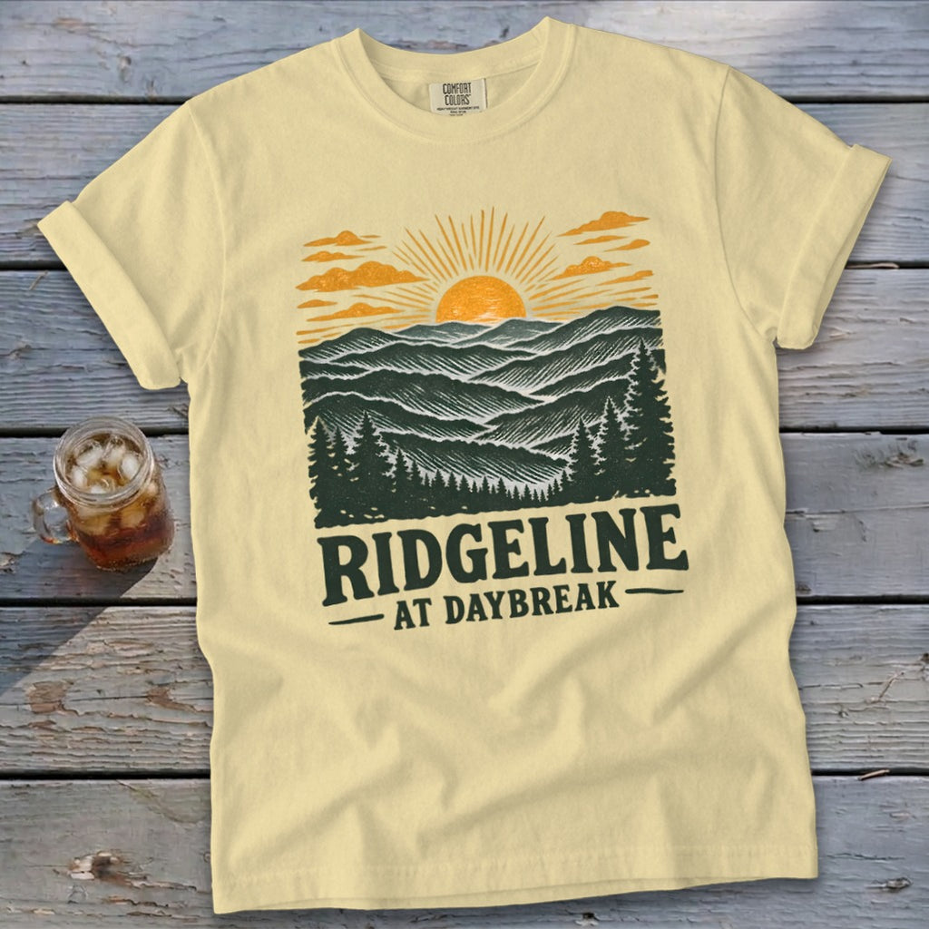 Light yellow t-shirt with a graphic of mountains and sunrise, text "RIDGELINE AT DAYBREAK".