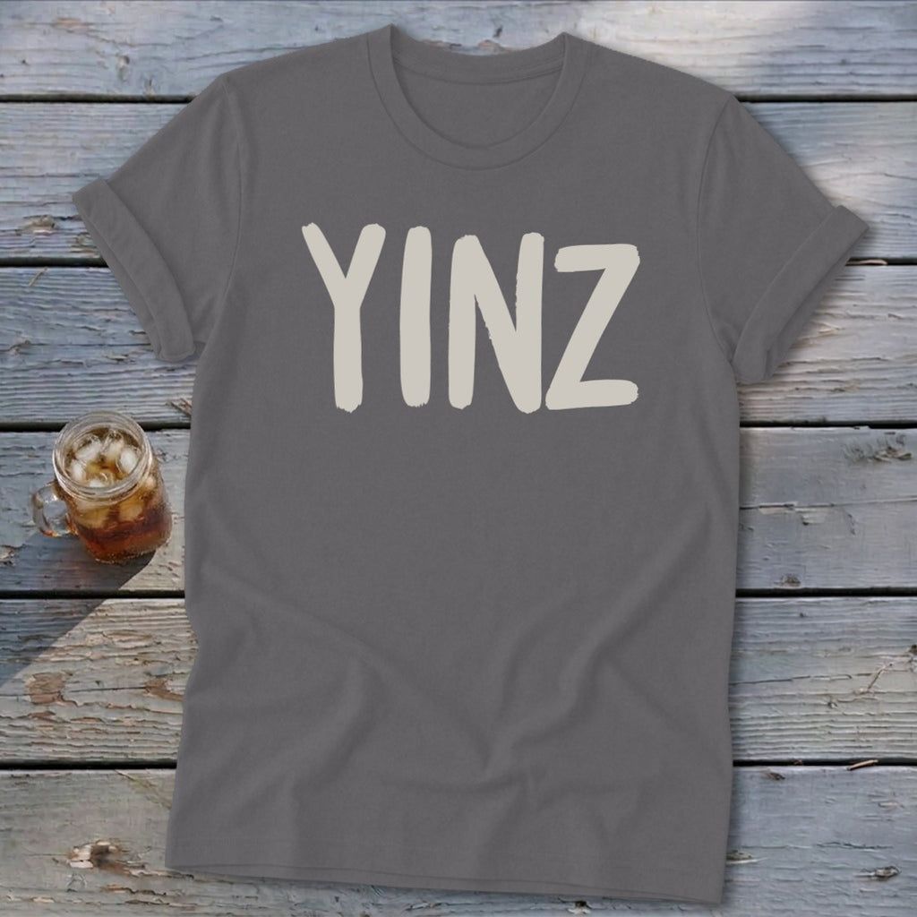 Grey t-shirt with "YINZ" in tan block letters, next to a mason jar drink.