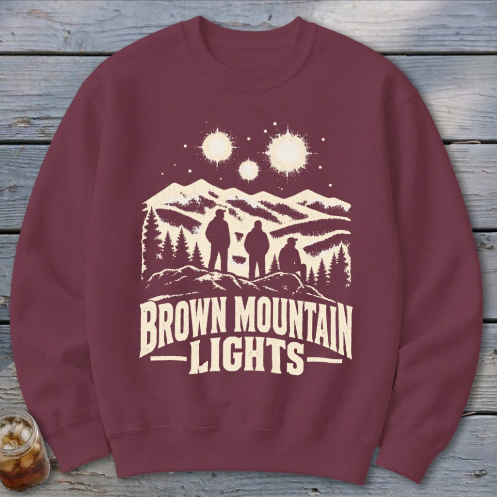 Maroon crewneck sweatshirt with a graphic of three figures looking at mountain lights.