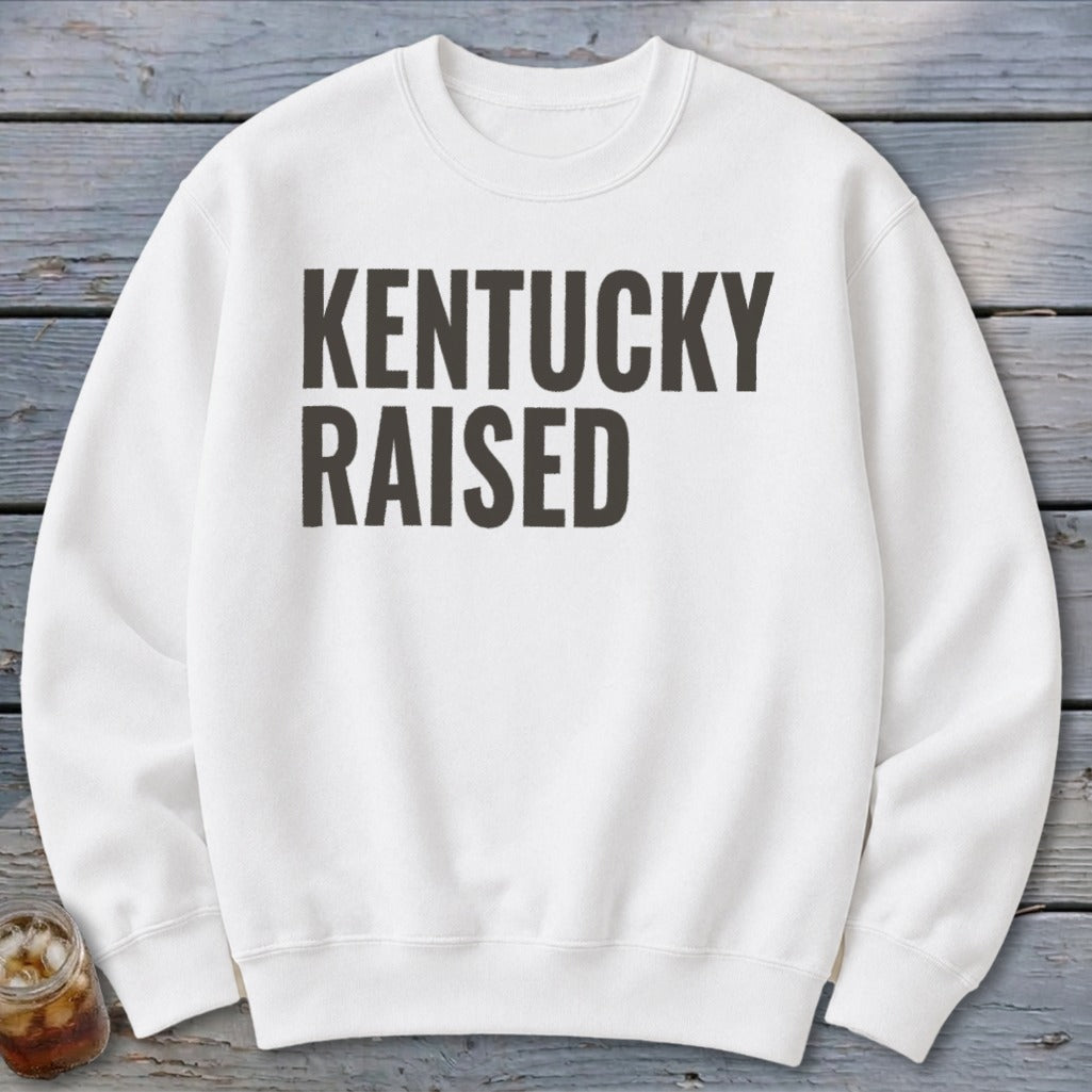 White crewneck sweatshirt with "KENTUCKY RAISED" text printed in dark gray.
