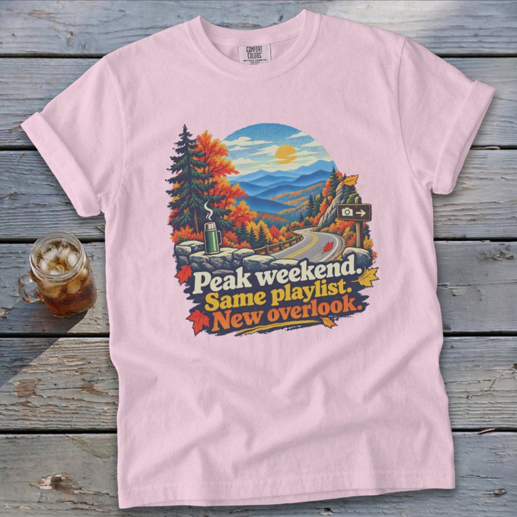 Pink t-shirt with "Peak weekend. Same playlist. New overlook." and mountain landscape.