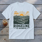White t-shirt with "RIDGELINE AT DAYBREAK" text and mountain sunrise graphic.