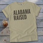 Khaki t-shirt with "ALABAMA RAISED" text in dark gray.