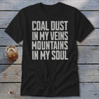 A black t-shirt printed with the white distressed text Coal Dust in My Veins Mountains in My Soul.