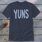 Dark blue t-shirt with "YUNS" in light blue, laid on weathered wood planks.