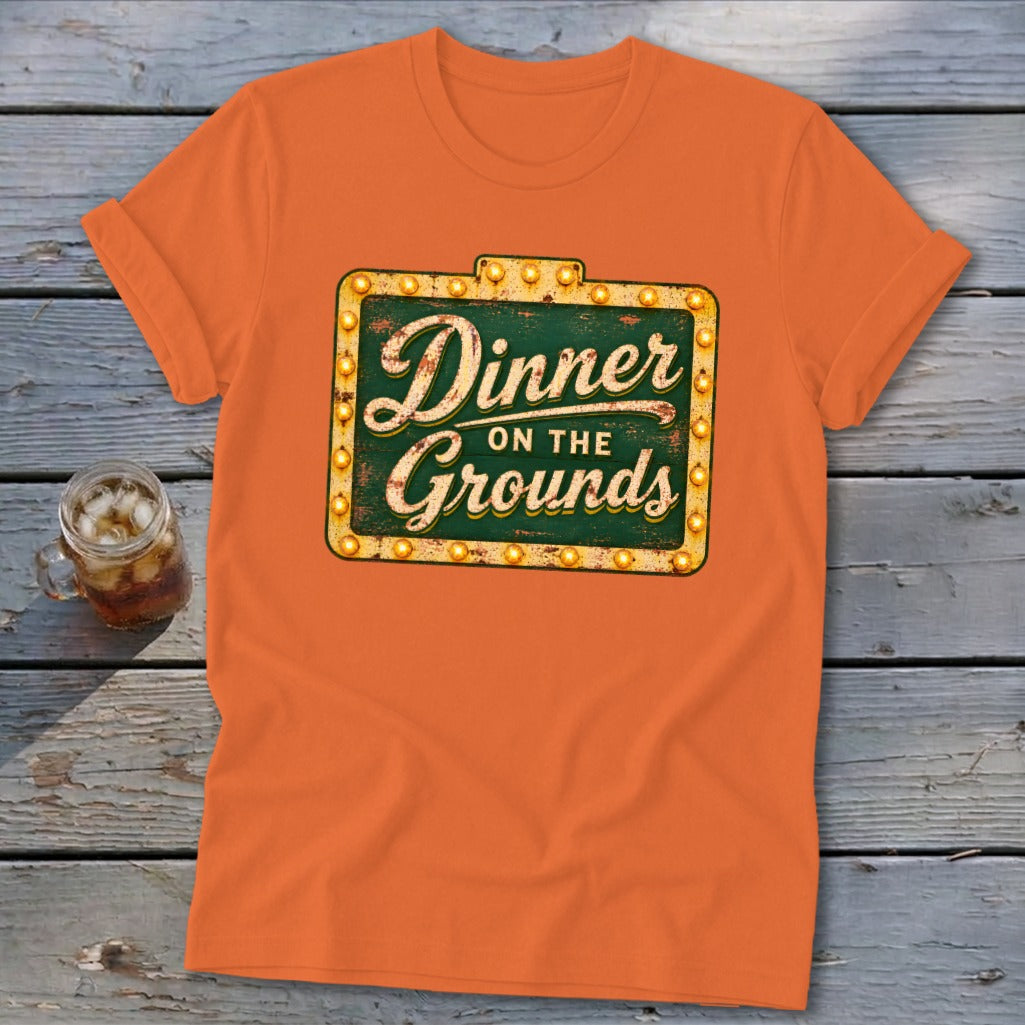 Orange t-shirt featuring a vintage lighted sign graphic with the text Dinner on the Grounds.