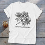 White t-shirt with a black botanical illustration of flowers and leaves, and the text "MOUNTAIN BORN".